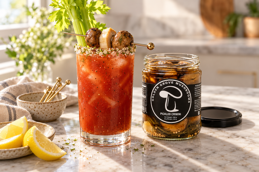 A Bloody Mary with a skewer of pickled crimini and a king oyster coin, beside an open jar of pickled crimini