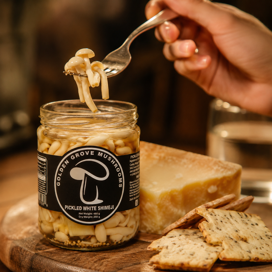 A fork lifting pickled white shimeji from an open jar beside cheese and crackers