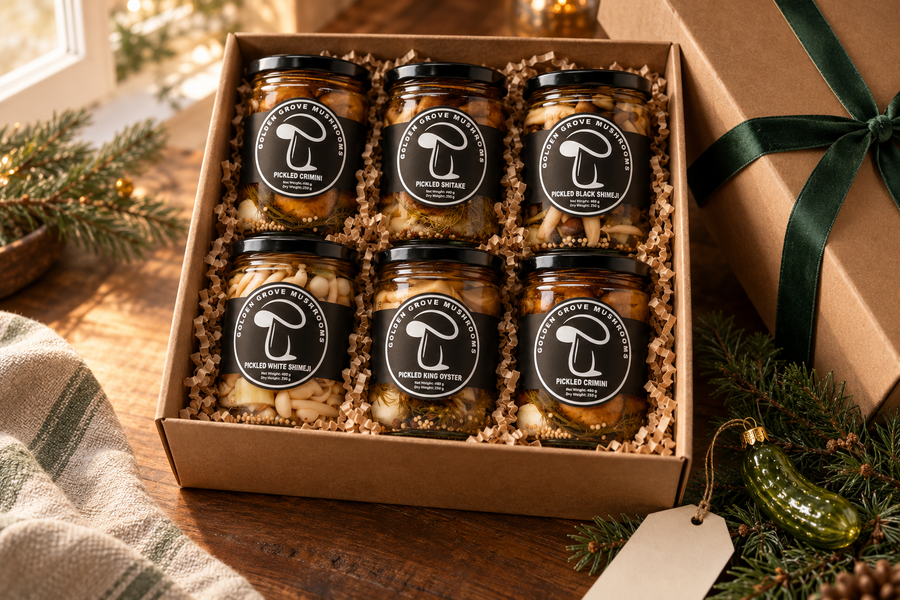 A gift box of six Golden Grove pickled mushroom jars in paper shred with a ribbon and a glass pickle ornament