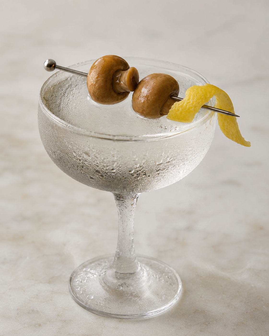 A pickled mushroom martini in a frosted coupe with two crimini on a cocktail pick