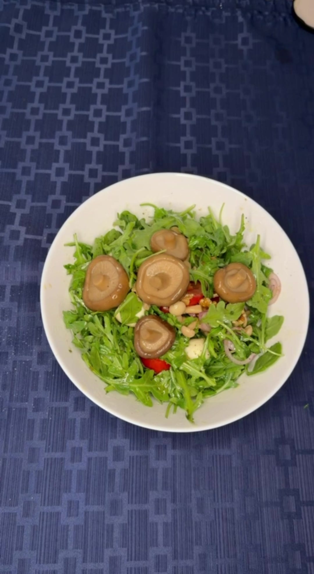 Arugula salad topped with pickled shiitake caps in a white bowl