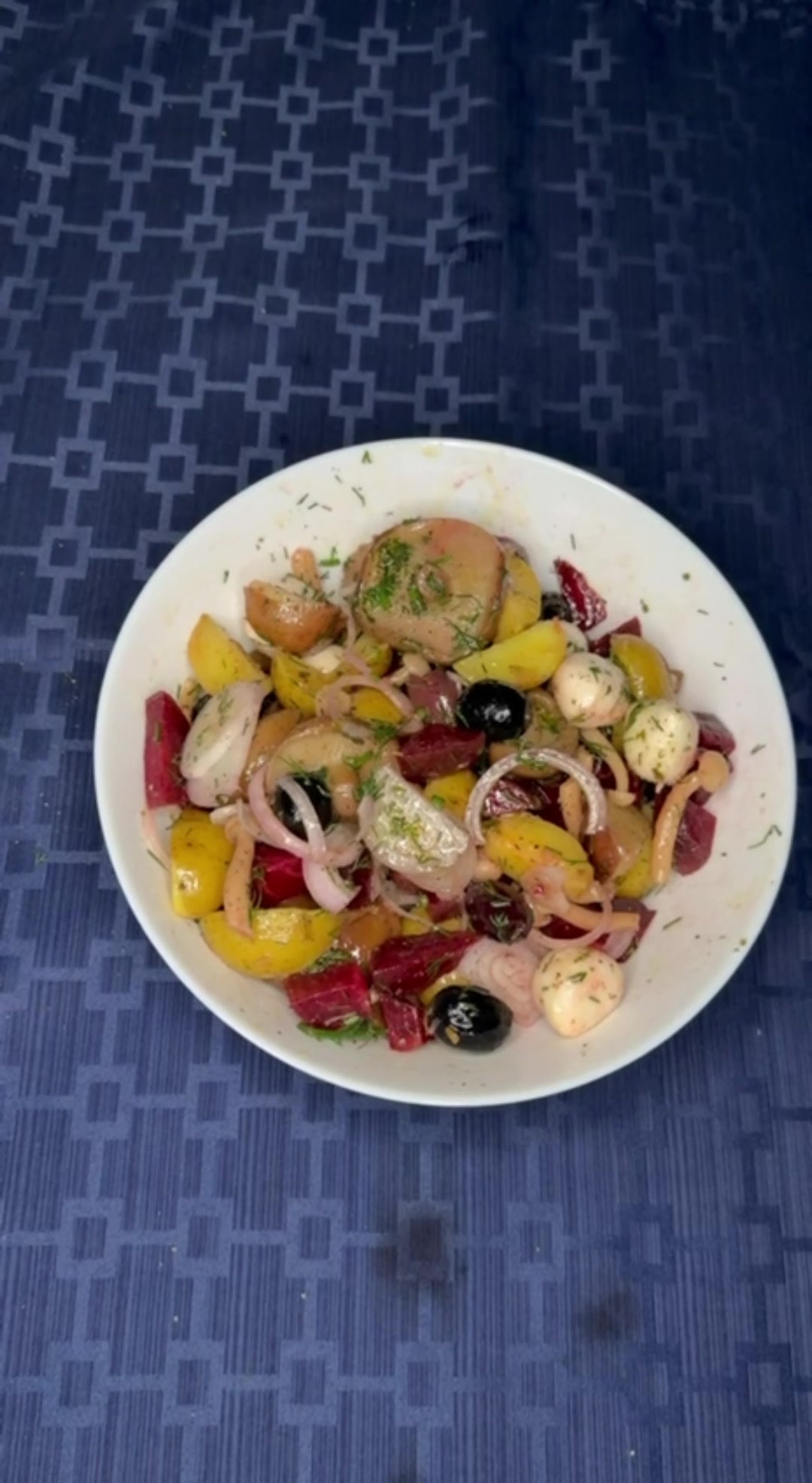 Beet and potato salad with pickled mushrooms, olives and mozzarella in a white bowl