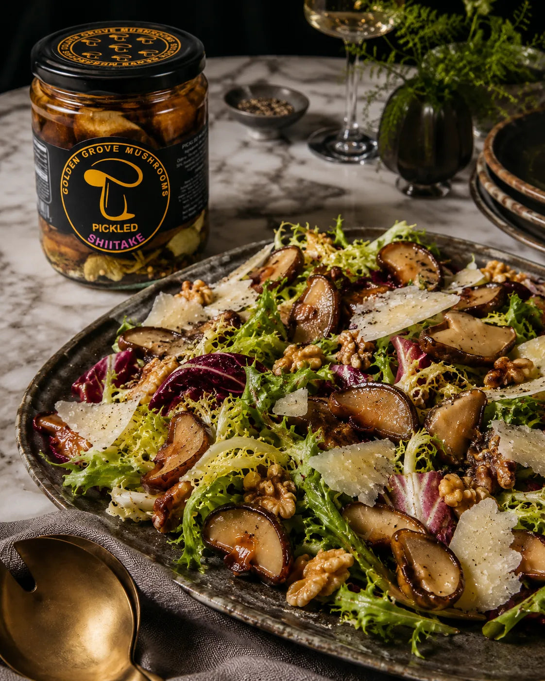 A platter of frisée and radicchio with sliced pickled shiitake, walnuts and shaved parmesan, beside a jar of pickled shiitake on marble.